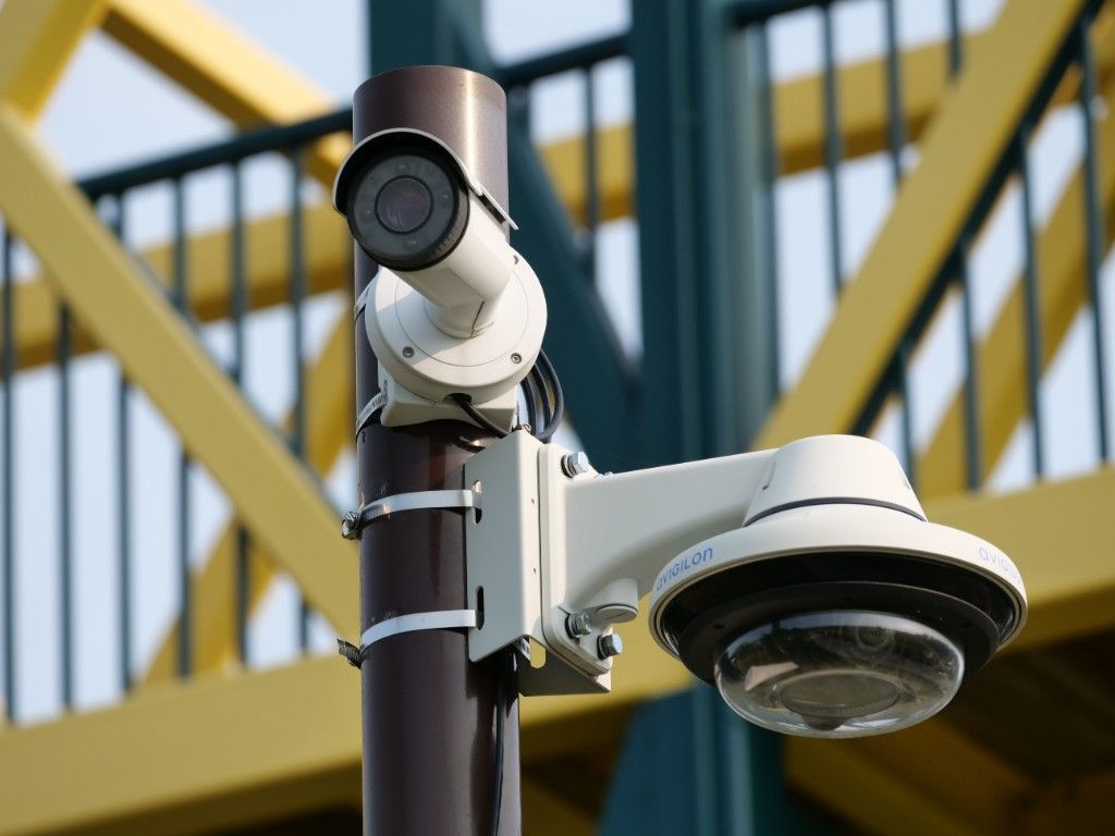 A bullet CCTV camera and a dome camera mounted on a pole beside a steel stairway.